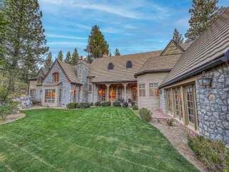 This stunning stone and wood home offers a picturesque setting surrounded by mature trees and a beautifully manicured lawn.