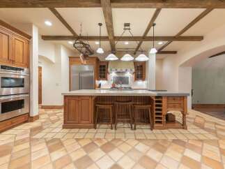 This spacious kitchen boasts a rustic charm with its exposed wooden beams and warm-toned cabinetry.