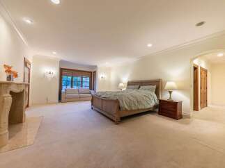 Experience luxurious living in this spacious master suite, featuring a grand fireplace and a cozy seating area by the bay window.