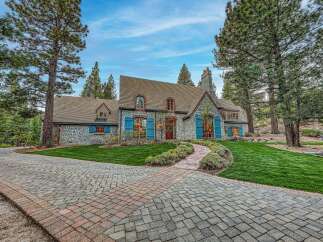 Experience the charm of this stone-clad residence, featuring vibrant blue shutters and a welcoming brick pathway leading to the entrance.