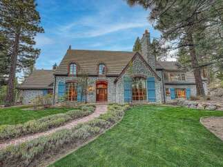 Experience luxury living in this stunning stone-clad home, featuring charming blue shutters and a classic French country architectural style.