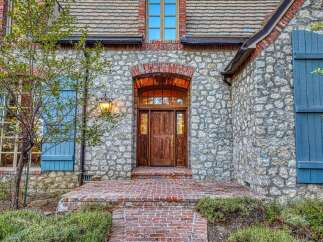 Step into charm with this exquisite stone home, featuring a welcoming brick pathway leading to a beautifully crafted wooden double door entrance.