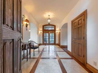 Step into a grand foyer featuring a stunning marble and wood inlay floor, leading to elegant double doors.