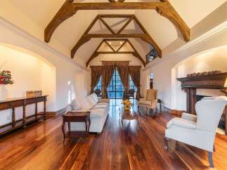 Experience luxurious living in this grand living room, featuring a stunning vaulted ceiling with exposed wooden beams and a majestic fireplace.