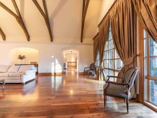 Experience luxurious living in this grand room featuring soaring vaulted ceilings with exposed wooden beams and expansive windows that flood the space with natural light.