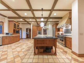 This spacious kitchen boasts a rustic charm with its exposed wooden beams and warm, terracotta tile flooring.