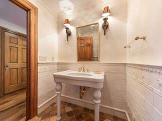 This charming bathroom features a pedestal sink with ornate brass fixtures, complemented by a decorative tiled wainscoting and a rustic terracotta tile floor.
