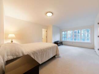 This spacious bedroom features a plush, neutral-toned carpet and large windows that offer a serene view of the surrounding trees.
