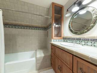 This charming bathroom features a classic white tiled bathtub and shower area, complemented by a decorative tile border.
