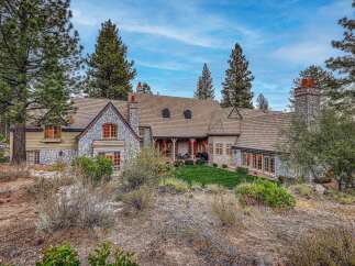 Nestled amidst tall pines, this stunning mountain home boasts a charming stone and wood exterior, complemented by a well-maintained lawn and a covered patio perfect for outdoor entertaining.