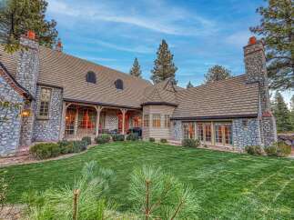 Experience luxury living in this stunning stone and wood-accented home, featuring a sprawling green lawn perfect for outdoor entertaining.