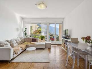 Experience breathtaking mountain and lake views from this stunning living room, featuring a comfortable sectional sofa and a modern dining area.