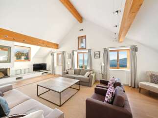 Experience breathtaking views from this spacious living room, featuring a vaulted ceiling with exposed wooden beams and large windows that frame the stunning landscape.