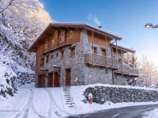 Experience the charm of a winter wonderland with this stunning stone and wood chalet nestled amidst snow-covered trees.