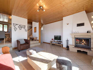 Experience cozy living in this charming living room, featuring a crackling fireplace and a rustic wooden ceiling.