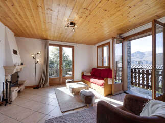 Experience cozy mountain living in this charming living room, featuring a rustic stone fireplace and a warm, wood-paneled ceiling.