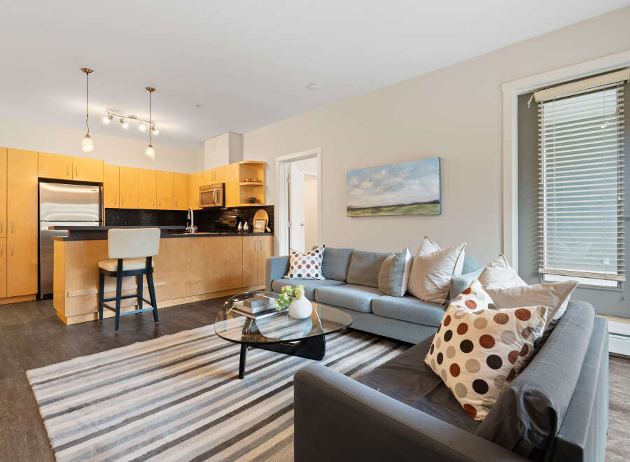 Step into this inviting open-concept living space, featuring a modern kitchen with sleek wooden cabinetry and a convenient breakfast bar.