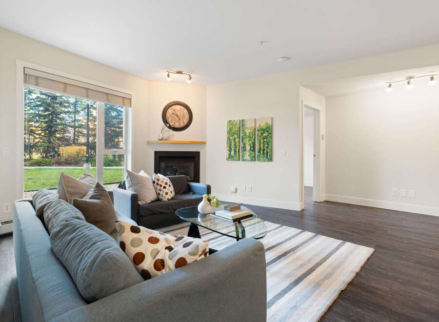 Step into this inviting living room, featuring a cozy fireplace and large windows that offer a view of the lush greenery outside.