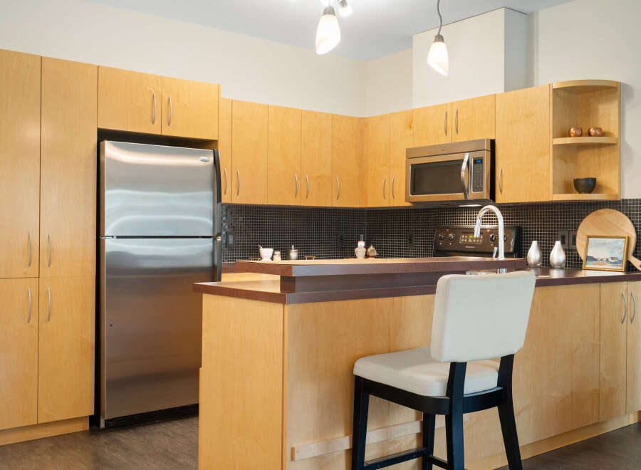 This modern kitchen boasts sleek, light wood cabinetry offering ample storage space, complemented by a stainless steel refrigerator and microwave.
