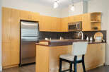 This modern kitchen boasts sleek, light wood cabinetry offering ample storage space, complemented by a stainless steel refrigerator and microwave.