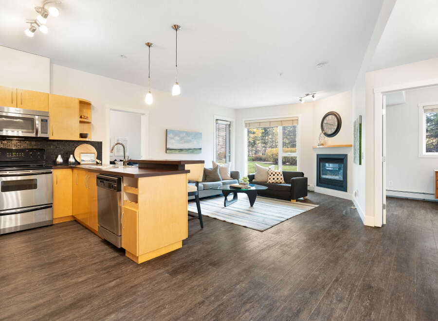 This modern open-concept living space features a sleek kitchen with stainless steel appliances and light wood cabinetry, seamlessly flowing into a comfortable living area.