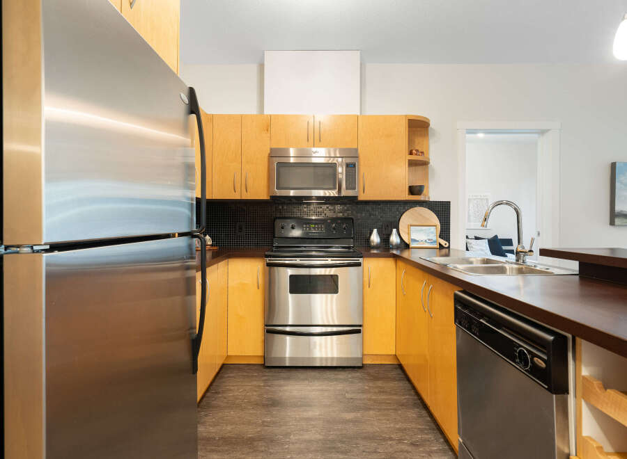 This U-shaped kitchen boasts sleek stainless steel appliances, including a refrigerator, microwave, and oven, complemented by warm, honey-toned cabinetry.