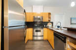 This U-shaped kitchen boasts sleek stainless steel appliances, including a refrigerator, microwave, and oven, complemented by warm, honey-toned cabinetry.