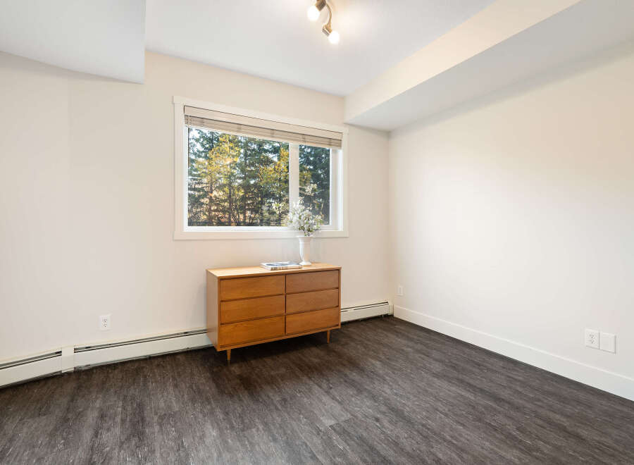 This room features a mid-century modern wooden dresser placed beneath a large window offering a view of lush trees.