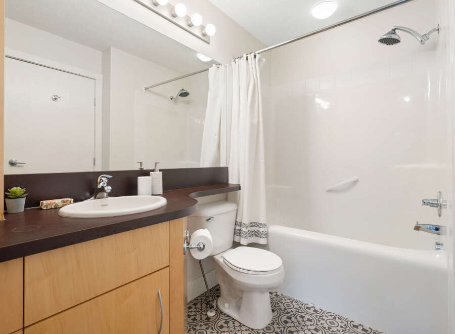 This modern bathroom features a sleek vanity with a white undermount sink and a dark countertop, complemented by light wood cabinetry.