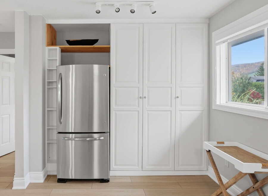 This kitchen features a sleek stainless steel refrigerator seamlessly integrated next to a wall of white cabinetry, offering ample storage.