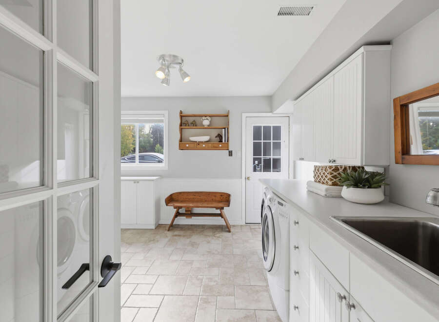 This spacious laundry room boasts ample storage with white shaker cabinets and a large countertop, perfect for folding clothes.