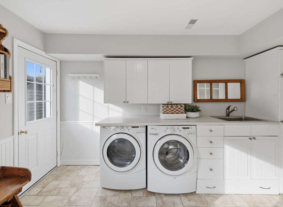 This bright and airy laundry room features a matching white washer and dryer set, complemented by ample white cabinetry for storage.