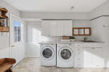 This bright and airy laundry room features a matching white washer and dryer set, complemented by ample white cabinetry for storage.