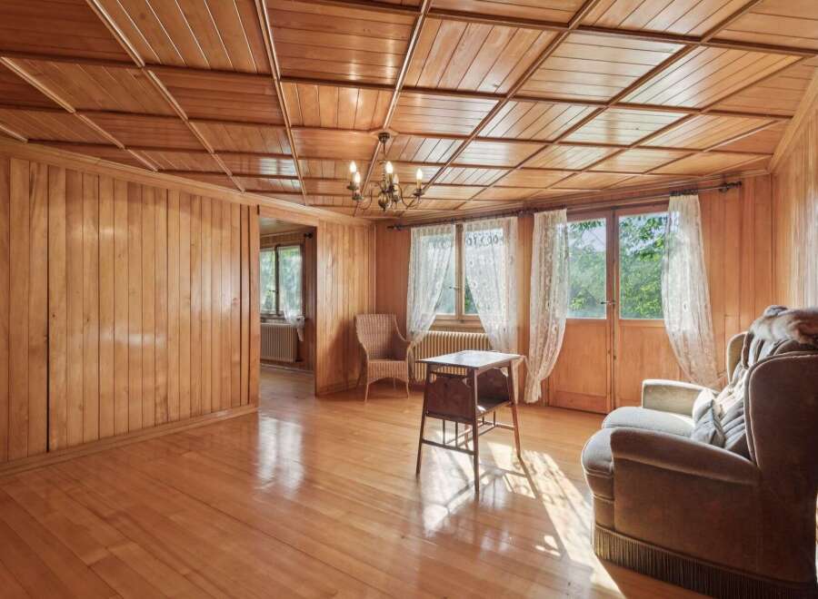 Step into a charming living space bathed in natural light, featuring warm, polished wood paneling on both the walls and the distinctive coffered ceiling.