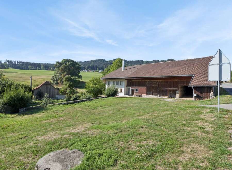 Discover this charming rural property featuring a spacious barn with traditional wooden doors and an attached white house with a prominent chimney.