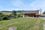 Discover this charming rural property featuring a spacious barn with traditional wooden doors and an attached white house with a prominent chimney.