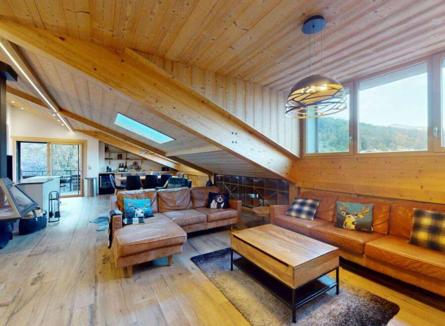Experience luxurious mountain living in this stunning chalet-style living room, featuring a modern fireplace and a vaulted wooden ceiling with integrated lighting.