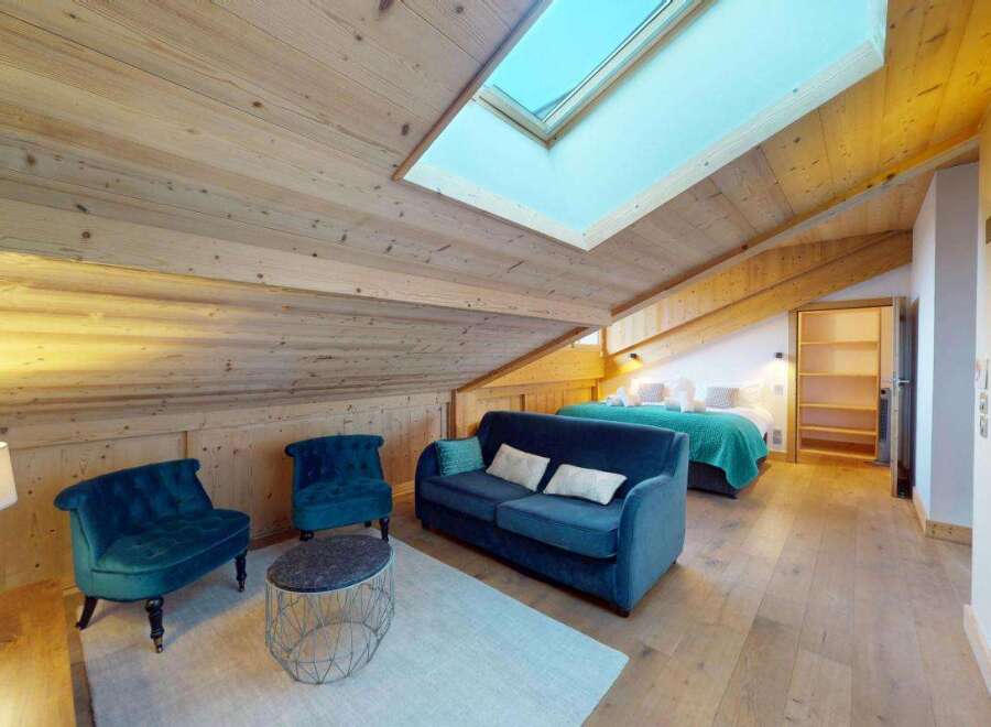 Experience cozy living in this charming attic bedroom, featuring a luxurious blue velvet sofa and two matching armchairs perfect for relaxation.