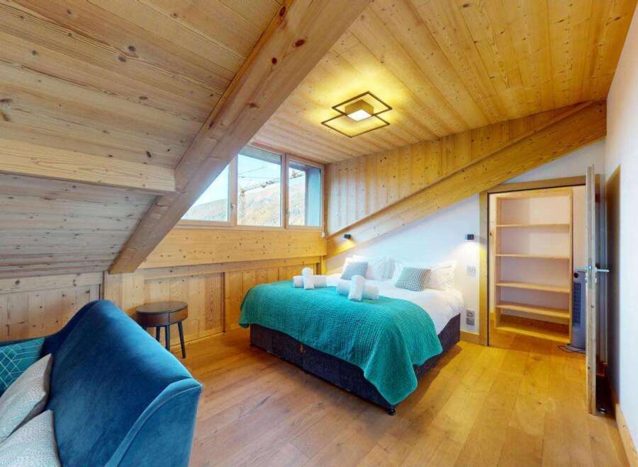 Experience cozy mountain living in this charming attic bedroom, featuring a plush blue sofa and a comfortable bed adorned with a vibrant teal throw.