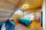 Experience cozy mountain living in this charming attic bedroom, featuring a plush blue sofa and a comfortable bed adorned with a vibrant teal throw.