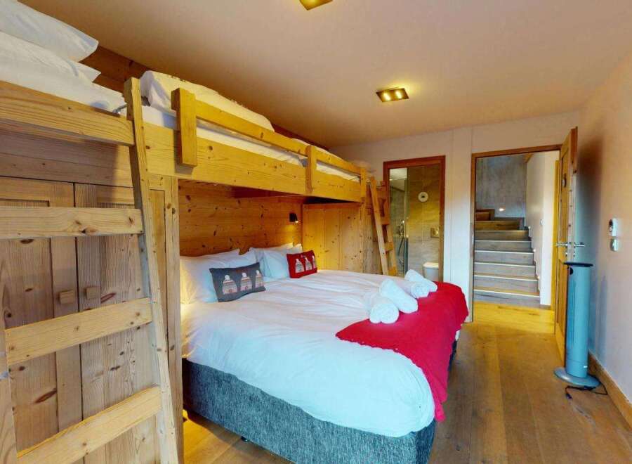Experience cozy comfort in this charming bedroom featuring a sturdy wooden bunk bed and a plush queen-size bed adorned with festive pillows and a vibrant red throw.