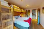 Experience cozy comfort in this charming bedroom featuring a sturdy wooden bunk bed and a plush queen-size bed adorned with festive pillows and a vibrant red throw.