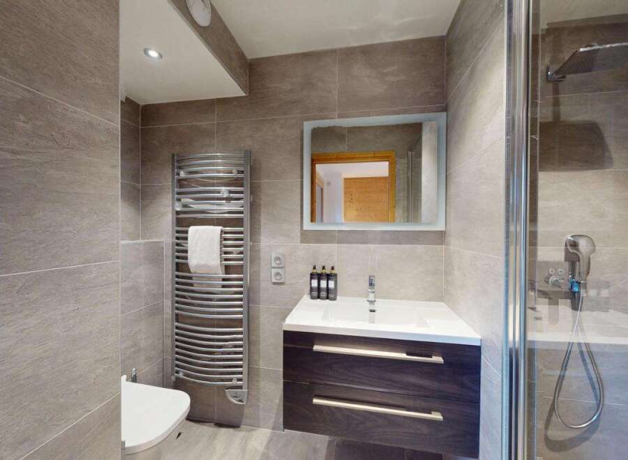 This modern bathroom features a sleek vanity with ample storage, a spacious walk-in shower with a rainfall showerhead, and a heated towel rack.