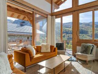 Experience breathtaking mountain views from this stunning living room, featuring a cozy orange sofa and a modern wood-burning stove.