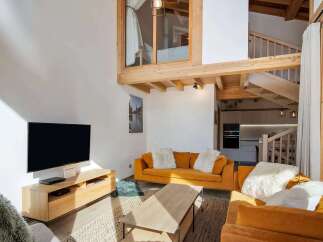 Experience modern alpine living in this stunning loft-style apartment, featuring a spacious open-plan living area with a cozy orange sofa and plush white cushions.