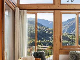 Experience breathtaking mountain views from this stunning living room, featuring a cozy orange sofa adorned with plush white and grey pillows.