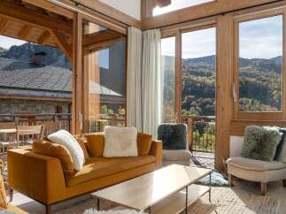 Experience breathtaking mountain views from this stunning living room, featuring a cozy orange sofa adorned with plush white and grey pillows.