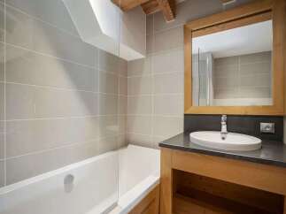This modern bathroom features a sleek bathtub with a glass screen, complemented by large, light grey tiled walls.