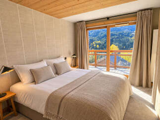 Experience breathtaking mountain views from this luxurious bedroom, featuring a comfortable king-sized bed adorned with plush pillows and a cozy throw blanket.