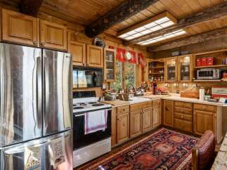 Experience rustic charm in this cozy log cabin kitchen, featuring warm wooden cabinetry and a large stainless steel refrigerator.